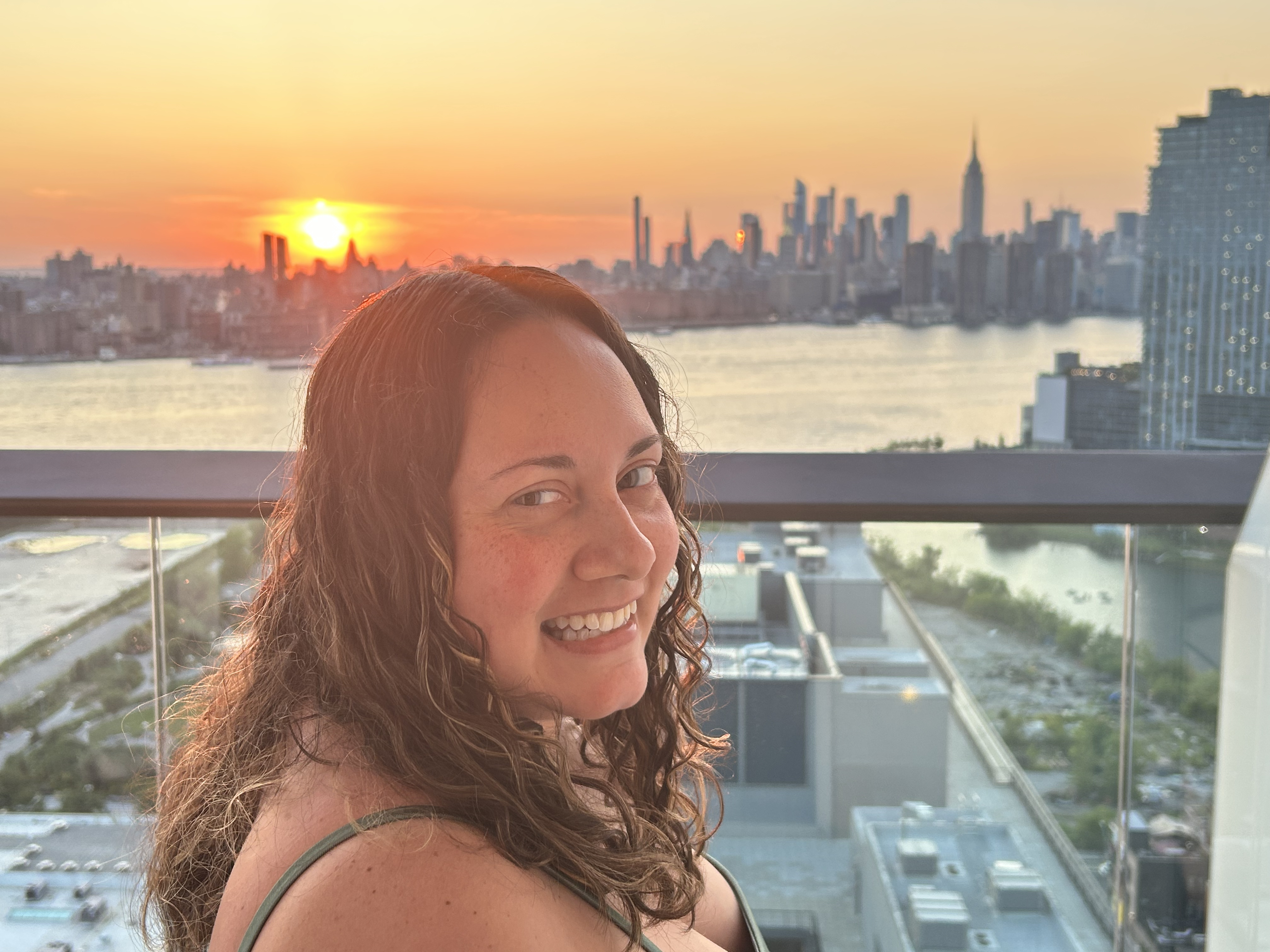 Brendi smiling with the New York City skyline at sunset